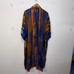 May include: A long, open-front robe with a vibrant pattern of blue and orange vertical stripes. The robe is hanging on a wooden hanger against a white wall. The sleeves are wide, and the fabric appears lightweight.