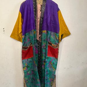 May include: A patchwork kimono robe with a vibrant color scheme. The robe features panels of purple, yellow, red, and teal fabrics. The design includes floral and geometric patterns, creating a unique and artistic garment.
