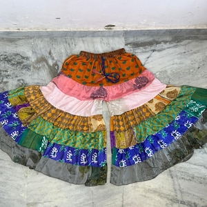 Puede incluir: Un pantalón palazzo patchwork colorido con cintura con cordón. Los pantalones presentan una variedad de telas estampadas en tonos naranja, rosa, amarillo, verde, azul y gris. El diseño de pierna ancha crea un estilo bohemio fluido.