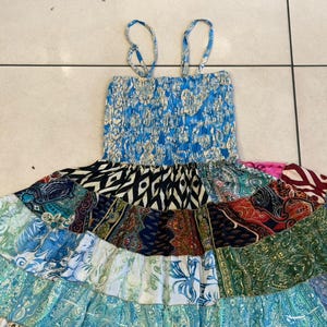 Puede incluir: Un vestido patchwork con un corpi&ntilde;o azul el&aacute;stico y tirantes finos. La falda presenta una variedad de telas estampadas en tonos azules, verdes, negros y rojos. El vestido est&aacute; dise&ntilde;ado para un estilo casual y bohemio.