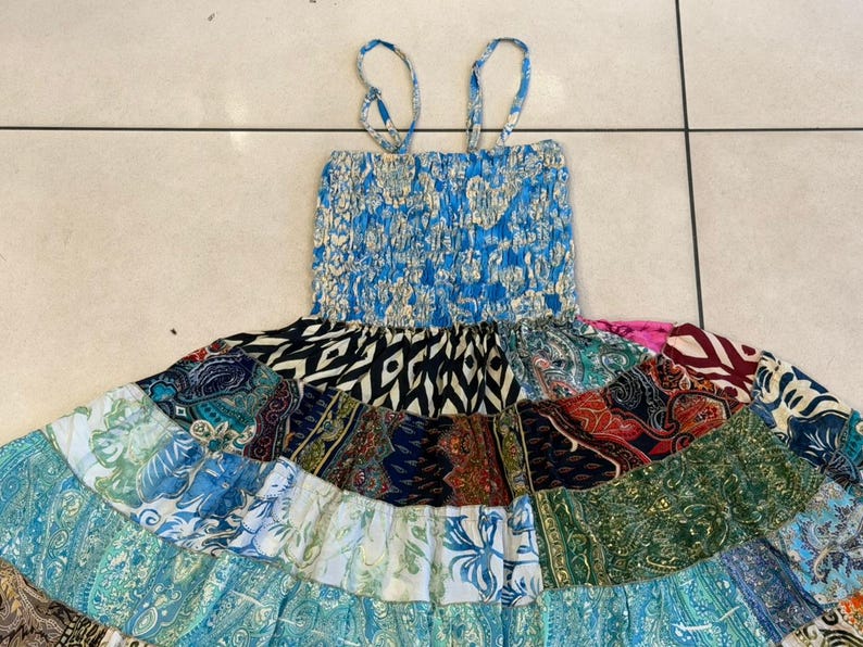 Puede incluir: Un vestido patchwork con un corpi&ntilde;o azul el&aacute;stico y tirantes finos. La falda presenta una variedad de telas estampadas en tonos azules, verdes, negros y rojos. El vestido est&aacute; dise&ntilde;ado para un estilo casual y bohemio.