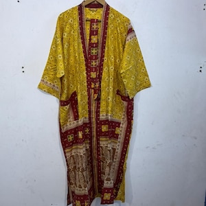 May include: A yellow kimono-style robe with a floral pattern and burgundy accents. The robe has a long, flowing design with pockets and a decorative border. The robe is hanging on a wooden hanger.