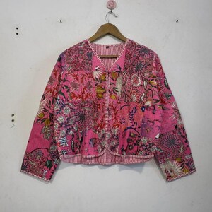 May include: A pink floral print jacket with a V-neck and long sleeves. The jacket features a patchwork design with various floral patterns in shades of pink, red, and yellow. The interior lining has a red and white striped pattern.