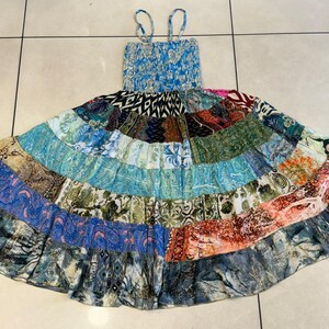 Puede incluir: Un vestido patchwork con un corpi&ntilde;o azul fruncido y tirantes finos. La falda presenta una variedad de parches de tela coloridos en tonos azules, verdes, naranjas y rosas. El vestido est&aacute; sobre una superficie embaldosada.