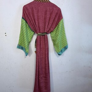 May include: A long, flowing robe in shades of burgundy, green, and blue, hanging on a wooden hanger. The robe features a paisley pattern on the main body, with patterned green sleeves and blue trim. The collar has a brown and tan animal print.