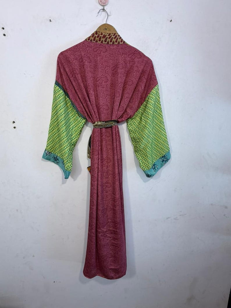 May include: A long, flowing robe in shades of burgundy, green, and blue, hanging on a wooden hanger. The robe features a paisley pattern on the main body, with patterned green sleeves and blue trim. The collar has a brown and tan animal print.