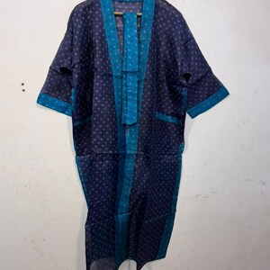 May include: A dark blue kimono-style robe featuring a repeating white geometric pattern. The garment has wide teal blue trim along the front opening, collar, and sleeve cuffs. A matching teal blue fabric belt is draped over the front of the robe.