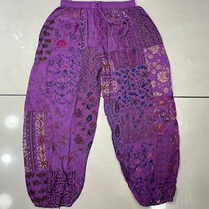 Può includere: Pantaloni viola con motivo e vita con coulisse. I pantaloni sono realizzati in un tessuto morbido e fluido e hanno uno stile bohémien.