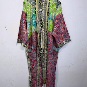 May include: A long-sleeved kimono robe featuring a patchwork design with vibrant paisley patterns in shades of lime green, magenta, deep purple, and black. The garment has an open front with a vertical border trim and is displayed on a wooden hanger.