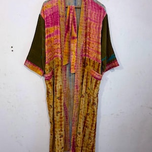 Könnte beinhalten: Ein langer, vorne offener Morgenmantel mit Patchwork-Design, leuchtend rosa und gelben Batikmustern auf den Vorderteilen und einfarbigen olivgrünen Ärmeln. Das Kleidungsstück verfügt über zwei Vordertaschen und einen passenden Bindegürtel.