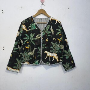 Könnte beinhalten: Schwarze Steppjacke mit einem lebendigen Dschungel-Print mit Zebras, Leoparden und Palmen. Die Jacke hat ein gestreiftes Futter und einen Besatz und hängt an einem Holzkleiderbügel.