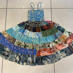 Puede incluir: Un vestido patchwork con un corpi&ntilde;o azul con estampado floral y tirantes finos. La falda es una vibrante mezcla de paneles de tela estampada en varios colores, incluyendo azul, verde, naranja y marr&oacute;n. El vestido tiene una silueta fluida y acampanada.