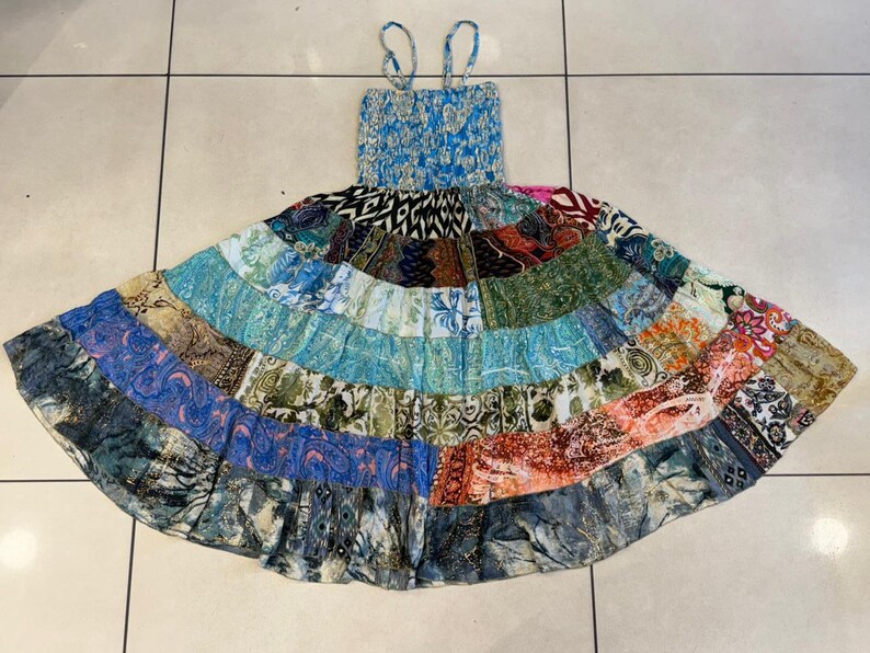 Puede incluir: Un vestido patchwork con un corpi&ntilde;o azul con estampado floral y tirantes finos. La falda es una vibrante mezcla de paneles de tela estampada en varios colores, incluyendo azul, verde, naranja y marr&oacute;n. El vestido tiene una silueta fluida y acampanada.