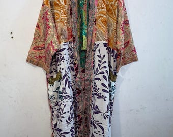 May include: A long-sleeved kimono-style robe featuring a patchwork design. The upper section displays an orange and pink paisley pattern, while the lower portion features a white fabric with a purple leaf and berry print. It has a front opening.