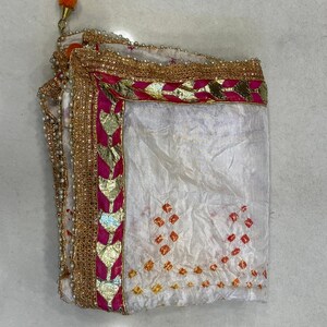 May include: White fabric with a decorative border featuring gold, pink, and pearl accents. The fabric has a pattern of orange and red diamond shapes. An orange tassel is attached to the corner.