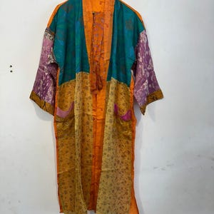 May include: A patchwork kimono robe in shades of orange, teal, yellow, and purple. The robe features a floral pattern on the lower half and sleeves, with solid teal and orange panels on the upper portion. Two pockets are visible.
