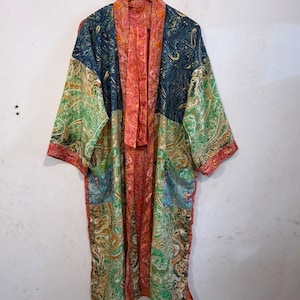 May include: A long-sleeved kimono robe featuring a patchwork design of various paisley patterns in vibrant shades of blue, green, orange, and red. The garment has an open front with a wide, solid orange-toned paisley border trim.