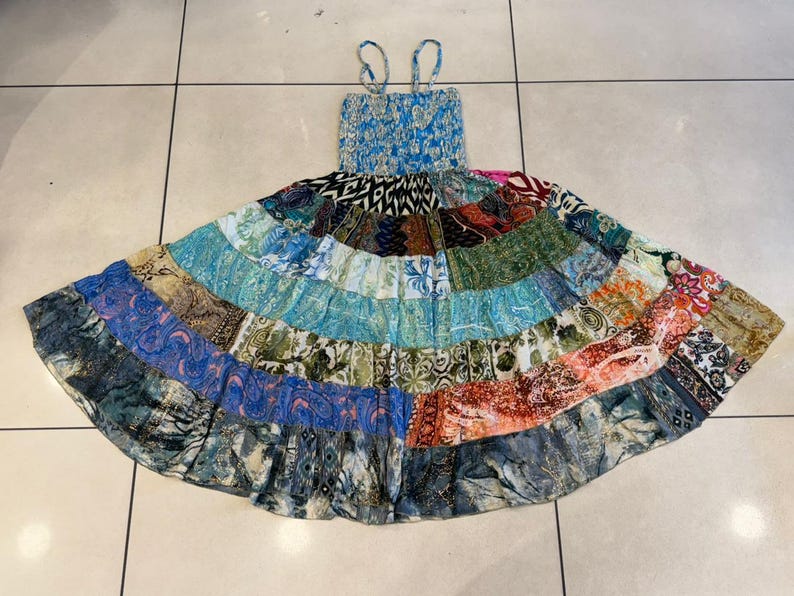 Puede incluir: Un vestido de verano patchwork con un corpi&ntilde;o azul con estampado floral y tirantes finos. La falda es una vibrante mezcla de parches de tela coloridos en varios patrones y tonos, incluyendo azules, verdes, naranjas y rosas. El vestido est&aacute; dise&ntilde;ado para un ajuste relajado.