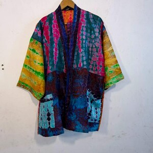 May include: A kimono-style jacket featuring a patchwork design with vibrant tie-dye patterns in shades of pink, teal, blue, and yellow. The garment has wide sleeves, an open front, and two front pockets, showcasing a mix of colourful fabric panels.
