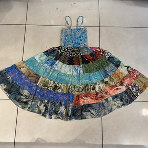Puede incluir: Un vestido patchwork con corpi&ntilde;o azul y tirantes finos. La falda est&aacute; hecha de varios patrones de tela en tonos de azul, verde, naranja y morado. El vestido est&aacute; dise&ntilde;ado con una silueta fluida y acampanada.