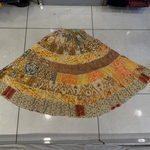 May include: A patchwork skirt with a variety of patterns and colors, including beige, brown, orange, and yellow. The skirt has a wide, flowing design and a patterned border. The skirt is made of multiple fabric panels.