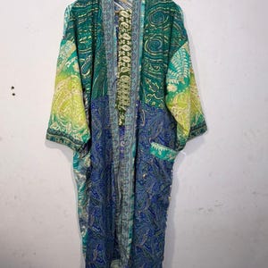 May include: A long-sleeved kimono robe featuring a patchwork design of various paisley patterns in shades of emerald green, lime green, and royal blue. The garment has an open front, a wide collar, and a single visible pocket on the lower left side.