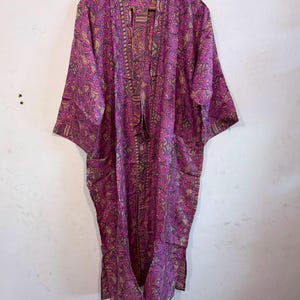 May include: A long-sleeved, open-front robe in a vibrant magenta pink hue, featuring an intricate, multi-colored paisley and floral pattern throughout. The garment has a straight, relaxed silhouette with wide sleeves and a matching patterned trim.