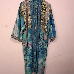 May include: A long-sleeved kimono robe featuring a vibrant blue, teal, and purple marbled pattern. The garment includes a contrasting dark blue paisley-printed trim along the front opening and sleeve cuffs, hanging from a wooden hanger.