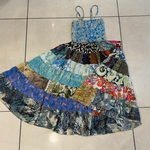 Puede incluir: Un vestido largo de patchwork con corpi&ntilde;o fruncido azul y tirantes finos. La falda presenta una variedad de telas estampadas en tonos de azul, verde, naranja y morado. El vestido est&aacute; dise&ntilde;ado para un ajuste relajado.