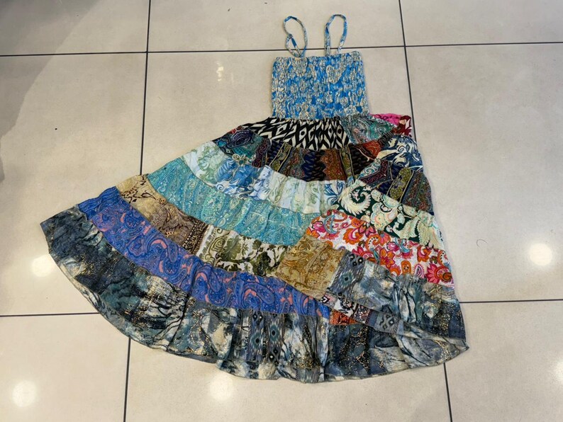 Puede incluir: Un vestido largo de patchwork con corpi&ntilde;o fruncido azul y tirantes finos. La falda presenta una variedad de telas estampadas en tonos de azul, verde, naranja y morado. El vestido est&aacute; dise&ntilde;ado para un ajuste relajado.