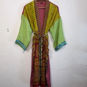 May include: A colorful, patterned kimono robe with a belt. The robe features a mix of colors, including green, yellow, red, and pink. The sleeves have a green pattern, and the body has a floral design. The robe is hanging on a wooden hanger.