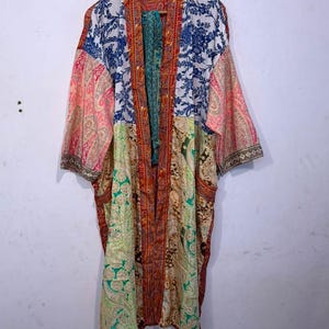 May include: A long-sleeved kimono robe featuring a patchwork design of various floral and paisley patterns in vibrant colors including blue, pink, green, and orange. The garment has a central vertical trim in a deep red and orange paisley print.