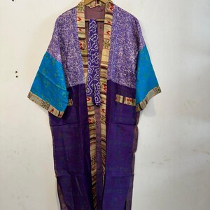 May include: A colorful kimono robe with a mix of patterns and colors. The robe features shades of purple, blue, and beige. The sleeves are a bright blue, and the robe is hanging on a wooden hanger.