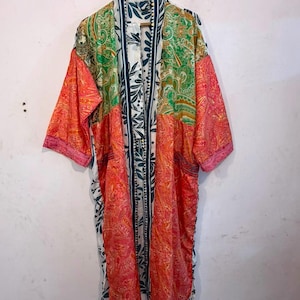 Może przedstawiać: Kimono z długim rękawem o patchworkowym wzorze w żywych odcieniach pomarańczu, zieleni i bieli. Odzież posiada skomplikowane wzory paisley oraz wyrazisty pionowy nadruk liści wzdłuż przedniego otworu i kołnierza.