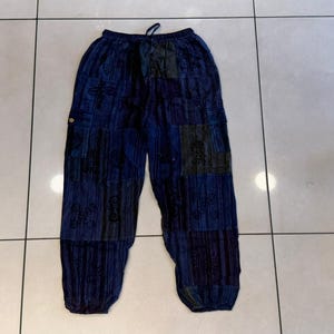 Puede incluir: Pantalones holgados en tonos azul oscuro y negro, con un diseño de patchwork que presenta varios patrones oscuros. Los pantalones tienen una cintura elástica con cordón ajustable y puños elásticos en la parte inferior de cada pierna.
