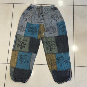 May include: Patchwork pants in shades of gray, blue, and gold. The pants feature various embroidered designs, including elephants, lions, trees, suns, and moons. The pants have a drawstring waist and a relaxed fit.