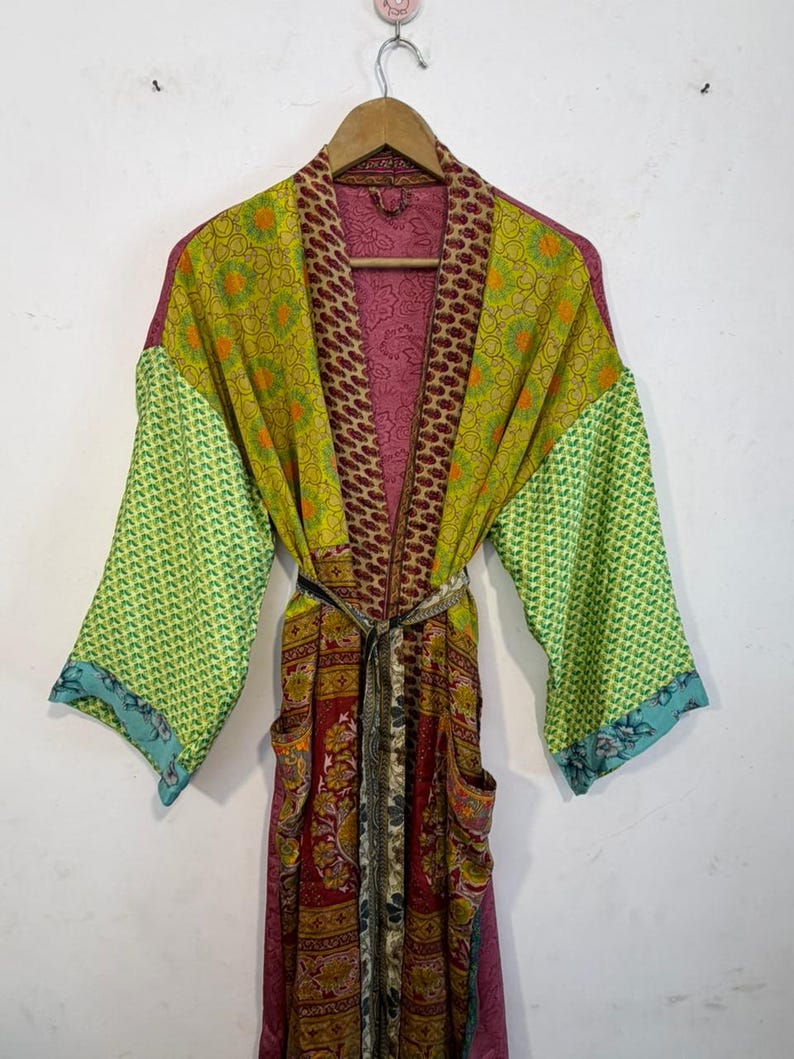 May include: A colorful, patterned robe with long sleeves and a belt. The robe features a mix of green, red, and purple fabrics with various designs. The sleeves have a green geometric pattern, and the robe has two pockets.