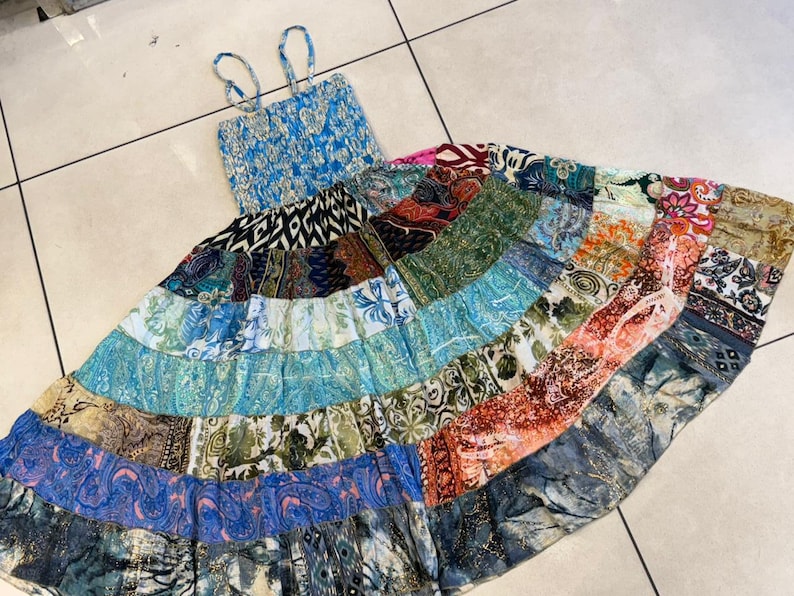 Puede incluir: Un vestido largo patchwork con corpi&ntilde;o azul y tirantes finos. La falda presenta una variedad de telas estampadas en tonos de azul, verde, naranja y rosa. El vestido est&aacute; dise&ntilde;ado para un ajuste relajado.