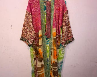 May include: A long-sleeved kimono robe featuring a patchwork design with various floral and abstract patterns in vibrant shades of pink, orange, green, and brown. The garment has an open front, wide sleeves, and a matching fabric belt hanging inside.