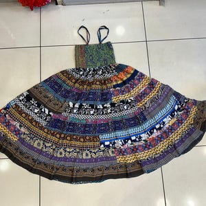 Peut inclure: Une robe maxi colorée à plusieurs couches avec un motif patchwork. La robe présente une variété de motifs floraux et géométriques dans des tons de bleu, vert, violet et jaune.