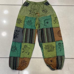 Könnte beinhalten: Patchworkhose in Grün-, Braun- und Grautönen mit verschiedenen Sonnen-, Mond- und Elefantenmotiven. Die Hose hat einen Kordelzugbund und eine lockere Passform.