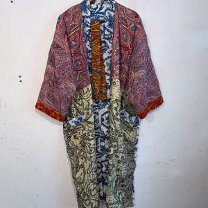 May include: A long-sleeved kimono-style robe featuring a patchwork design with various patterns. The upper section displays a pink and red paisley print, while the lower portion features a cream and black intricate scrollwork pattern.