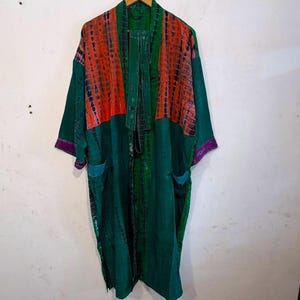May include: A long-sleeved kimono-style robe featuring a deep green base color with vibrant orange tie-dye panels on the upper front. The garment includes two front pockets, purple trim on the sleeve cuffs, and a matching tie belt for closure.