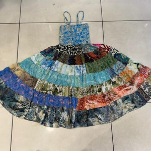Puede incluir: Un vestido patchwork con un corpi&ntilde;o azul el&aacute;stico y tirantes finos. La falda est&aacute; hecha de varios parches de tela en tonos azules, verdes, naranjas y dise&ntilde;os estampados. El vestido est&aacute; dise&ntilde;ado para un ajuste relajado.