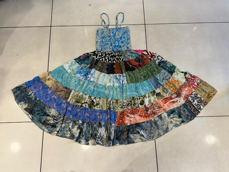 Puede incluir: Un vestido patchwork con un corpi&ntilde;o azul el&aacute;stico y tirantes finos. La falda est&aacute; hecha de varios parches de tela en tonos azules, verdes, naranjas y dise&ntilde;os estampados. El vestido est&aacute; dise&ntilde;ado para un ajuste relajado.