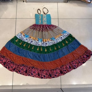 May include: A colorful, patchwork maxi dress with a turquoise bodice and a tiered skirt. The skirt features panels of various patterns and colors, including blue, green, orange, and pink. The dress has a flowing, bohemian style, perfect for warm weather.
