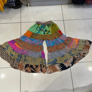 May include: Patchwork palazzo trousers in a wide-leg style. The trousers are made from various patterned fabrics in green, blue, orange, pink, and brown. They have a drawstring waistband.