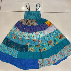 Può includere: Un abito patchwork multicolore con uno schema di colori blu, verde e viola. L'abito ha una gonna a strati con una varietà di motivi floreali.