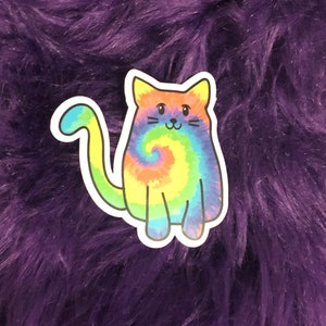May include: A colorful tie-dye cat sticker with a rainbow swirl pattern. The cat is sitting with its tail curled around its body.