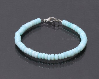 Op de afbeelding: Een lichtblauwe armband van opaal kralen met een zilveren sluiting. De armband is gemaakt van kleine, ronde kralen en is ongeveer 18 cm lang.